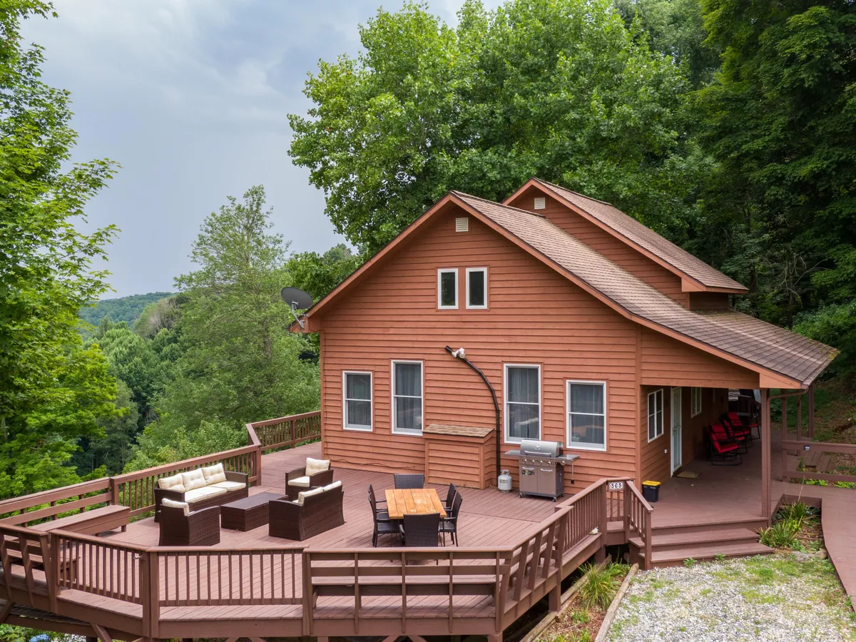 A wooden deck with ample outdoor seating, dining table, and surrounding trees forms a perfect backdrop for social gatherings or quiet mornings in nature. The communal seating invites groups to gather and connect.