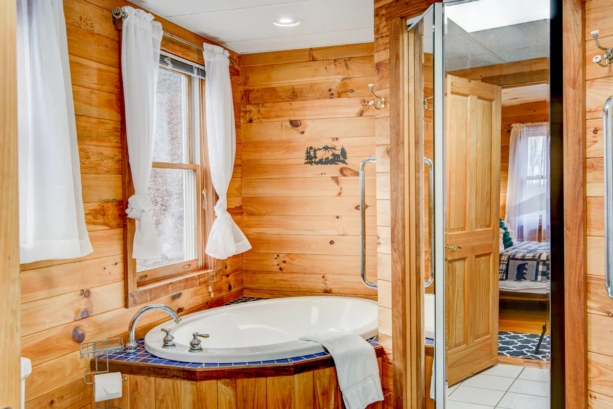 This image highlights a bathroom with a jacuzzi tub surrounded by wooden walls, a mirrored cabinet, and white curtains. The soft lighting and tranquil atmosphere evoke a spa-like experience.