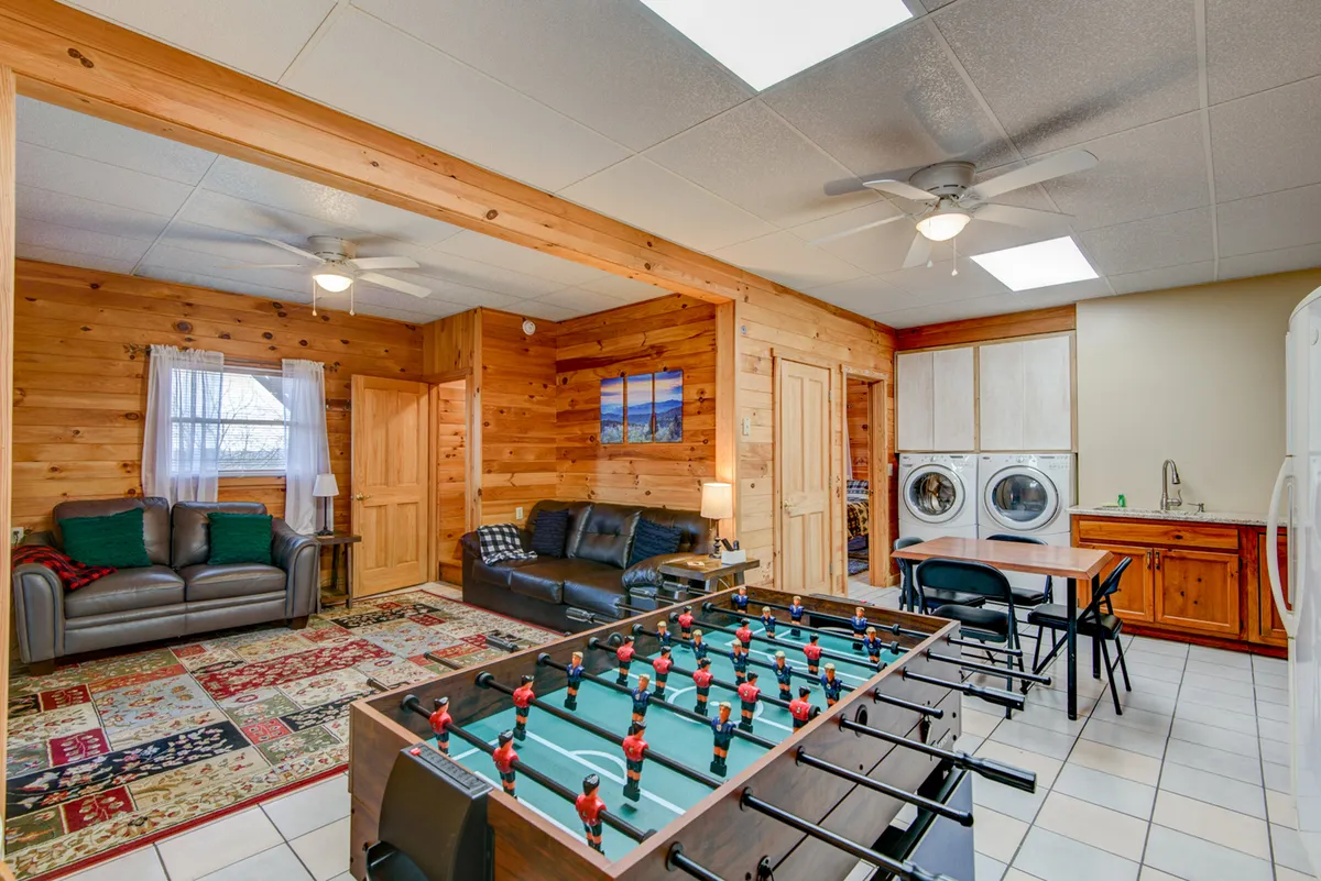 A spacious game and laundry area featuring a foosball table, sofas, dining table, and a clearly visible laundry set, creating a relaxed, multipurpose environment for socializing and daily routines.