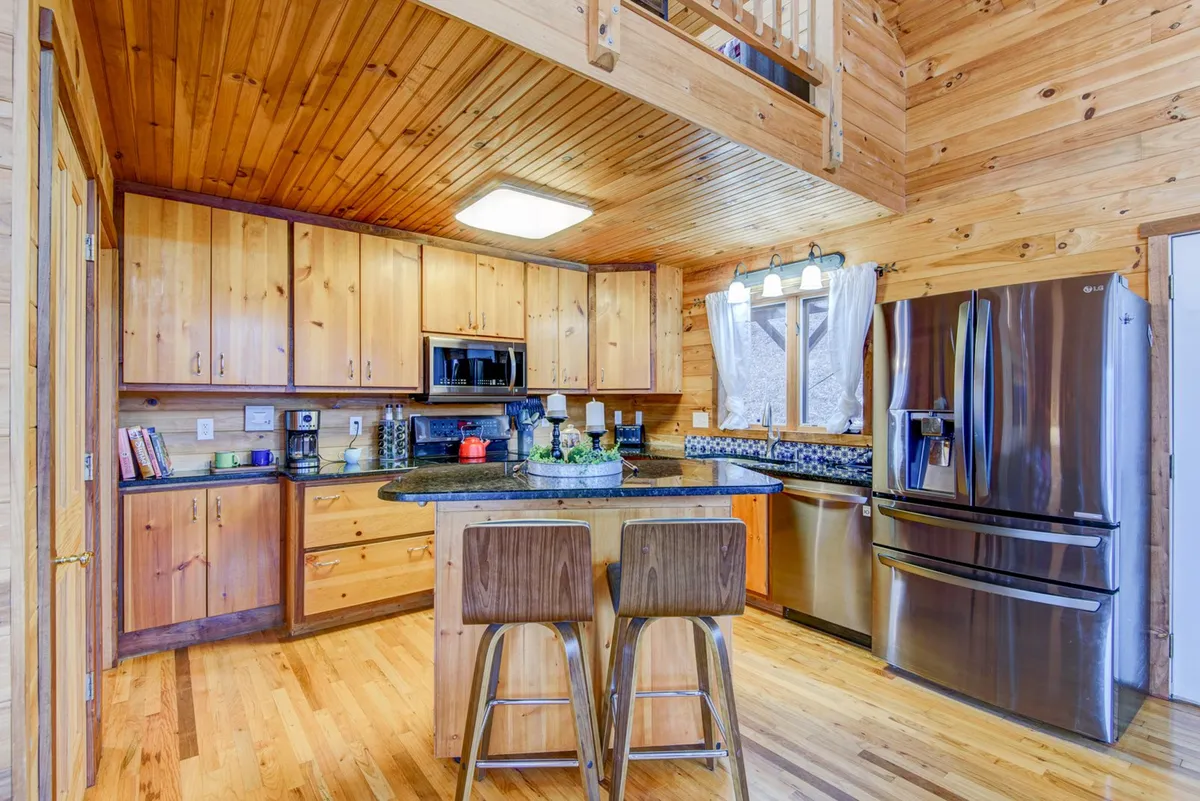 A warmly lit, open kitchen featuring a central island, stainless steel appliances, wooden cabinets, and stylish light fixtures. The space radiates an inviting atmosphere, perfect for cooking family meals or entertaining guests.