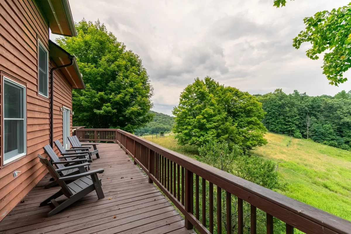 A generous wooden deck with classic red rocking chairs overlooks a panorama of distant hills and treetops, surrounded by the serenity of the forest. The peaceful setting offers an inviting space for families to relax, sip morning coffee, or simply take in the views.