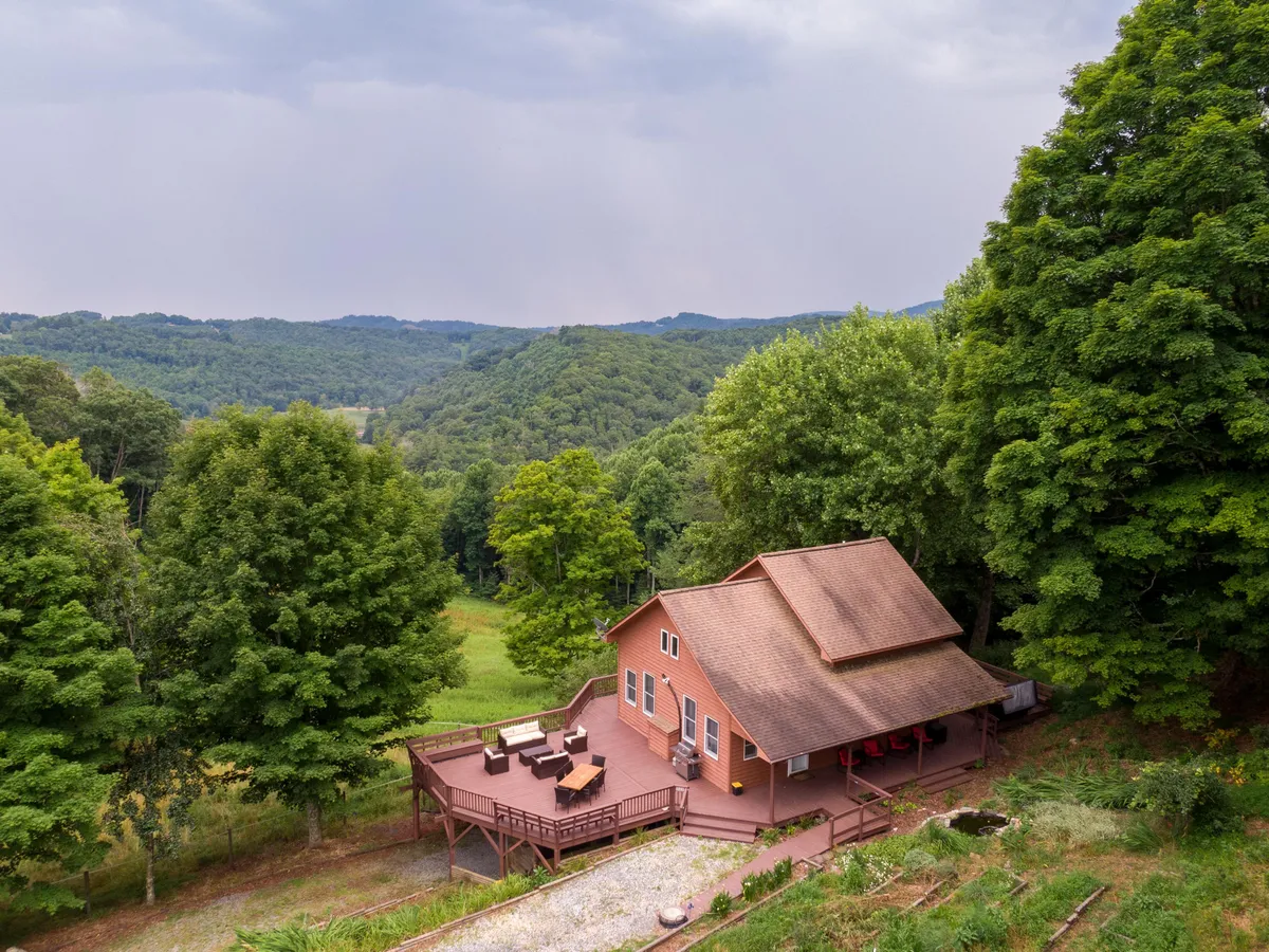 The home’s exterior with a wide deck, set against a backdrop of green trees and rolling hills. The space includes areas for lounging and gathering, connecting the house to the expansive High Country environment.