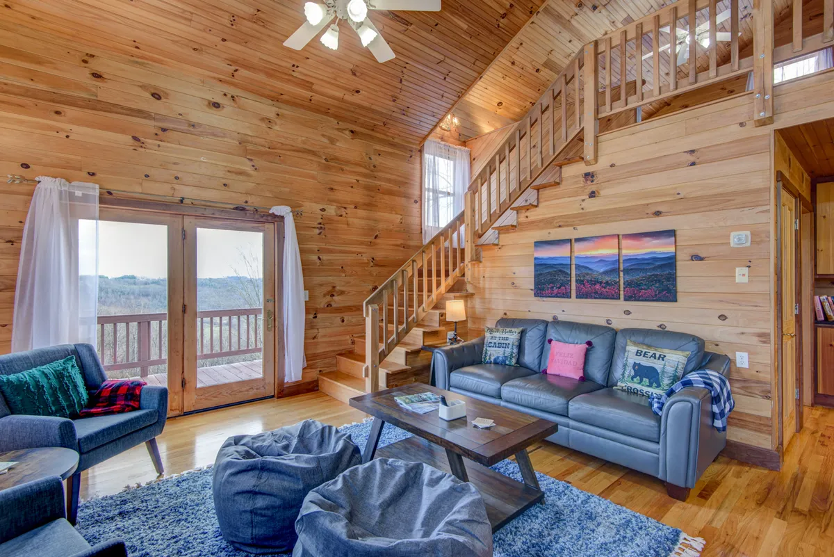 An inviting interior lounge features a cozy sofa, bean bags, stairs, and expansive windows that let in natural light. The space is designed for relaxing, reading, game nights, or simply enjoying the views from inside.