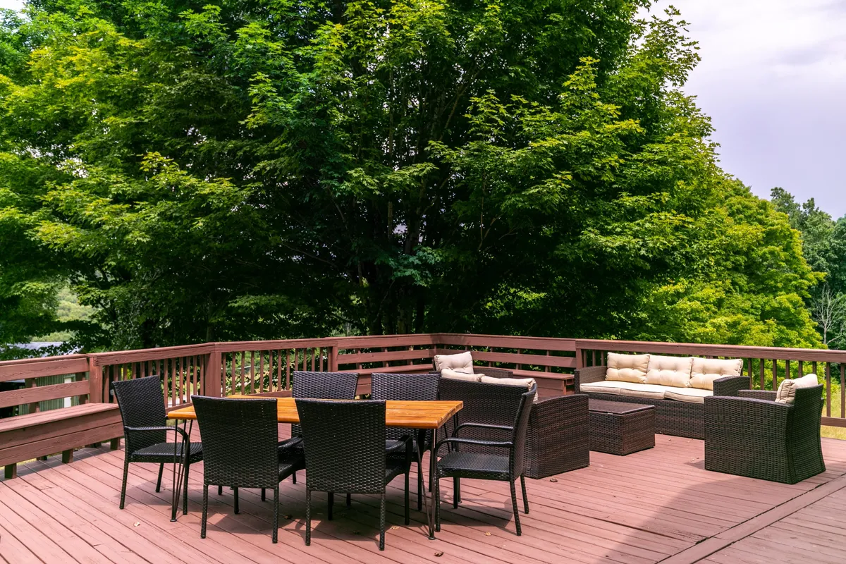 This image showcases an inviting outdoor dining area surrounded by lush green trees, with a comfortable couch and chairs arranged to accommodate a group. The atmosphere is welcoming and set up for gatherings, meals, and casual conversation in a scenic setting.